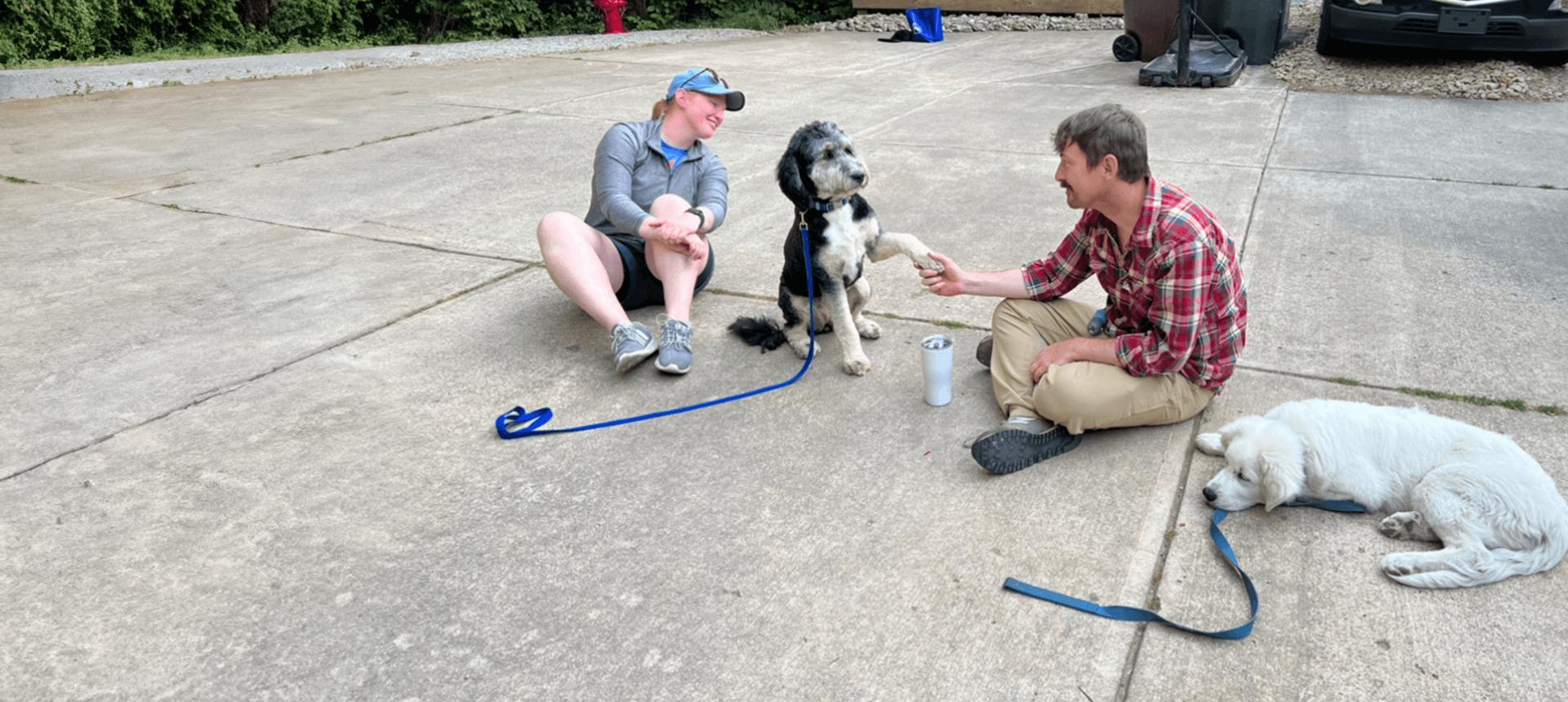 Two men sitting on the ground with a dog.